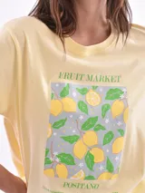 Remera color amarillo claro con estampado de limones, hojas y flores en tonos verdes y grises.