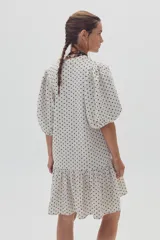 Vestido corto color blanco con estampado de lunares negros, escote en V, mangas cortas abullonadas y falda con volantes.