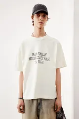 Remera de corte holgado en punto de algodón color crema, con cuello redondo acanalado y estampado con texto en el frente.