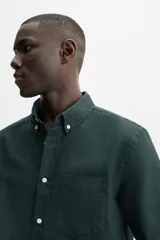Camisa azul marino de corte regular fit, confeccionada en tejido de algodón Oxford. Tiene cuello abotonado, manga larga con puños abotonados, bolsillo de parche en el pecho y cierre frontal con botones.