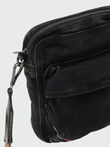 Bandolera pequeña de tela denim negra con efecto desgastado, con múltiples bolsillos frontales y cierre superior de cremallera. Incluye correa ajustable de tela tejida en tono verde oliva/marrón.