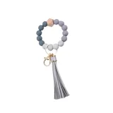 Llavero tipo pulsera con cuentas redondas en tonos grises, aro y gancho metálico dorado y borla plateada.
