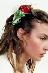 Pinza para el pelo color crema con forma de flor roja y hojas verdes en relieve.