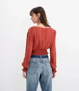 Blusa color ladrillo con escote redondo con ajuste, mangas largas con aberturas en los hombros y elástico en la cintura.