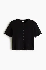 Saco corto negro de punto fino suave con cuello redondo, mangas cortas y botonadura frontal. Tiene ribete festoneado en tapeta, mangas y bajo.
