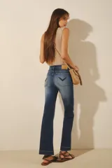 Jean de mujer color azul oscuro, tiro alto, corte oxford (o campana moderada) con desgaste localizado y bordado de alas negras en los bolsillos traseros.