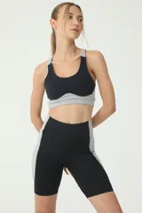 Top deportivo de compresión en color negro y gris, con costuras blancas y logo retro en la espalda, diseñado para entrenamientos intensos.