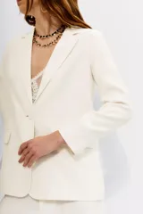 Blazer color blanco hueso, con solapas de muesca, cierre frontal con un botón y bolsillos delanteros con solapa.