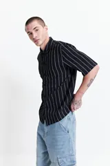 Camisa de manga corta con fit oversize a rayas verticales blancas sobre fondo negro, de estilo rústico.