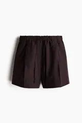 Short marrón de lino con cintura elastizada y cordón ajustable. Presenta pliegues frontales, bolsillos laterales y corte holgado.