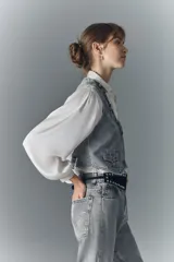 Chaleco vintage de denim rígido color gris, con botones metálicos grabados, bolsillos con solapa en el frente y tira de ajuste en la espalda.