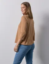 Blusa blanca de poliéster y elastano, con cuello a la base, escote en V y mangas tres cuartos. Presenta dos bolsillos frontales con cierre metálico dorado.