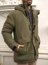 Campera verde militar con capucha, cierre frontal con cremallera y broches, bolsillos laterales con solapa y puños ajustables con velcro.