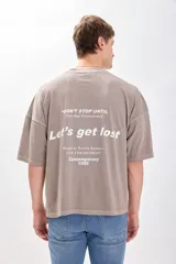 Camiseta manga corta color beige con estampa en la espalda que dice "DON'T STOP UNTIL YOU ARE UNSTOPPABLE", "Let's get lost", "BASED IN SOUTH AMERICA LIVE THE MOMENT Contemporary 1995". Corte amplio y recto, más ancha que larga y sin ajuste al cuerpo.