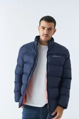 Campera inflada azul marino de nylon con cuello alto, cierre frontal con cremallera, bolsillos laterales con cierre y logo estampado en el pecho. El modelo usa talle M.