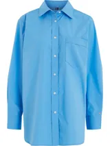 Camisa celeste de popelín de algodón orgánico, corte oversize con hombros caídos, cuello inglés, bolsillo de parche en el pecho y logo bordado en la manga.