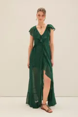 Vestido largo cruzado color verde esmeralda con estampado de puntos dorados. Presenta escote en V con volados en los hombros y en el borde del cruce, y un lazo para ajustar a la cintura.