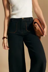 Jean de corte wide leg y tiro alto, color negro con costuras en contraste color ocre. Presenta bolsillos delanteros y traseros con detalle de pespunte, y ruedo ancho con costura decorativa.