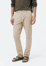 Pantalón de vestir color beige, de corte slim fit, con bolsillos laterales y traseros. Se ajusta a la cintura con cinturón de cuero marrón.