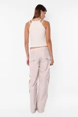 Pantalón cargo color arena de corte recto y tiro bajo, con recortes y presillas dobles en la cintura. Tiene acceso mediante cierre de nylon y botón personalizado, seis bolsillos laterales y dos en la espalda con tapa y botón snap a presión.