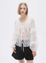 Blusa blanca traslúcida de encaje con mangas largas abullonadas y volados.