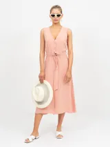 Vestido midi sin mangas de color salmón, con escote en V y abotonadura frontal. Cuenta con un lazo en la cintura para ajustar el calce.