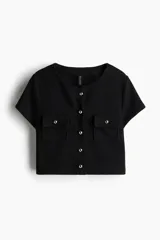 Top corto negro en tejido de punto waffle, con cuello redondo, manga corta, cierre frontal con botones dorados y bolsillos de parche con solapa y botón en el pecho.