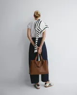 Bolso tipo tote grande color marrón, con doble asa de mano y correa larga extraíble. Interior con dos compartimentos y bolsillo central con cierre.