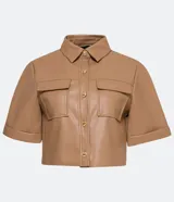Camisa de manga corta confeccionada en material sintético color beige. Tiene cuello camisero, cierre de botones en forma de corazón, dos bolsillos con solapa y corte cropped.