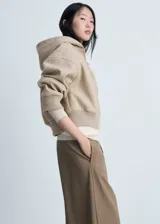 Chaqueta beige con capucha, cierre frontal con cremallera, puños y cintura elásticos.