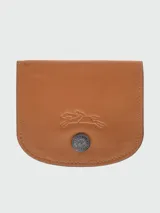 Tarjetero tipo monedero de cuero color camel, con solapa redondeada y cierre a presión metálico con logo grabado. Presenta un logo de caballo al galope grabado en relieve en la parte frontal.