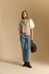 Chaleco tejido sin mangas color blanco roto, con cuello redondo y cartera frontal de botones. Presenta un punto calado con textura.