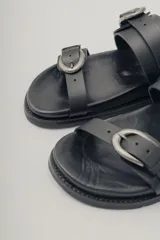 Sandalia plana de cuero color caramelo, estilo 'slide' o 'dos tiras', con hebillas ajustables de metal dorado en cada tira.