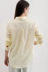 Camisa blanca a rayas verticales negras, de corte clásico, con cuello camisero y mangas largas con puños abotonados.