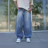 Jean de hombre, color celeste desgastado, corte ultra ancho (baggy) y tiro alto. Presenta un parche de cuero marrón con logo en el reverso de la cintura y un estampado circular blanco en el bolsillo trasero derecho.