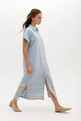 Vestido largo de lino en color celeste, con cuello camisero, manga corta y cierre frontal con botones. Presenta bordados decorativos en contraste en la pechera y en el ruedo.