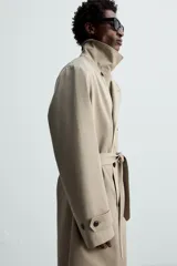 Trench largo regular fit color beige confeccionado en tejido italiano repelente al agua. Tiene cuello con solapas de pico, manga larga con puño ajustable con trabilla, bolsillos de vivo en cadera, bolsillo interior, cinturón del mismo tejido en cintura, bajo con abertura en centro espalda y cierre frontal de botonadura cruzada.