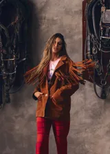 Campera marrón de gamuza con corte masculino, hombros marcados y caída recta. Presenta flecos largos en la espalda y mangas.