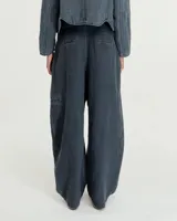 Pantalón de lino color gris gastado, con pinzas, silueta comba en piernas, bolsillos ojal en pierna izquierda y espalda. Largo hasta los tobillos y tiro medio.