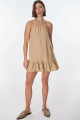 Vestido corto color beige, con escote halter, tirantes finos y falda con volados.