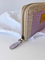 Billetera pequeña con cierre metálico, cuerpo principal de cuero lila texturizado y ribetes en color crema. Presenta un parche de cuero marrón con la palabra "chowie" escrita en cursiva.