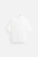 Camisa blanca de corte relaxed fit, con cuello solapa, manga corta y cierre frontal con botones.