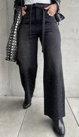 Pantalón de jean negro de corte recto, con tachas plateadas y cinturón fino con hebilla metálica.