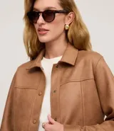 Campera estilo safari o sobrecamisa de mujer, color marrón camel, confeccionada en tejido que simula gamuza o cuero sintético. Presenta cuello camisa, cierre frontal de botones a presión, y cuatro bolsillos frontales con tapa (dos en el pecho y dos a la altura de la cadera). Tiene costuras visibles que definen el diseño.
