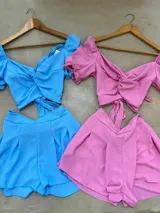 Conjunto color ocre compuesto por un top corto con escote en V, mangas cortas abullonadas y nudo en el frente, y un short de tiro alto con cintura elastizada. Incluye un cinturón blanco con tachas y hebilla dorada.