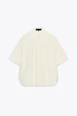 Camisa color crema de cuello solapa y manga corta con vuelta. Tiene un bolsillo de parche en el delantero, bajo asimétrico con aberturas laterales y cierre frontal con botones.
