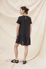 Vestido negro corto con cuello redondo, mangas cortas y falda con volantes.