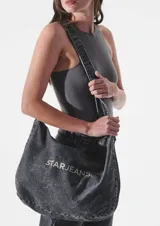 Bolso tipo tote de denim celeste con lavado ácido y estampado del logo "STARJEANS" en negro. Tiene correa larga regulable y cierre superior.