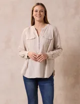 Blusa color beige de lino y rayón, con cuello a la base, escote en V y abertura con botones. Tiene bolsillos en la parte delantera y mangas largas regulables con presilla y botón.