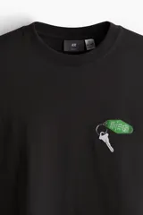 Remera negra de corte holgado y mangas cortas, con cuello redondo y estampado pequeño de llave de hotel en el pecho.